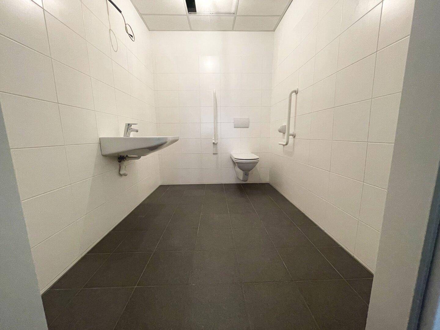 Modernes, barrierefreies Badezimmer mit weißen Fliesen, dunklem Boden und Haltegriffen für Komfort.