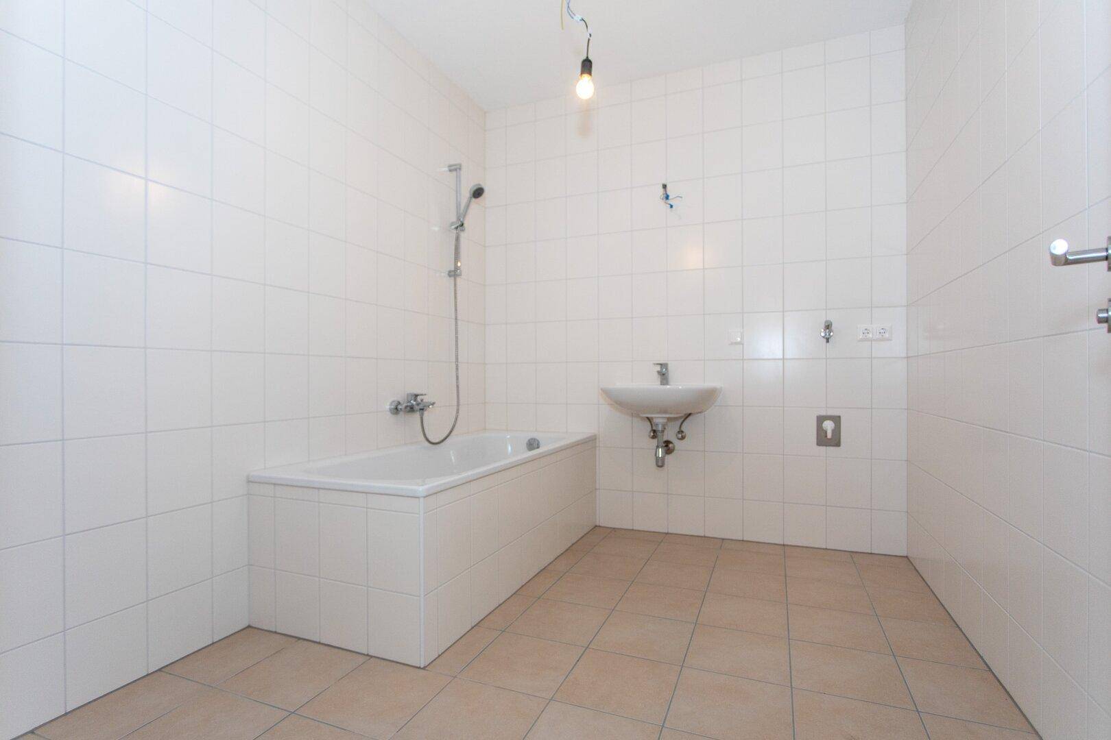 Modernes Badezimmer mit weißen Wandfliesen, beigefarbenem Boden und einer Badewanne mit Duschfunktion.