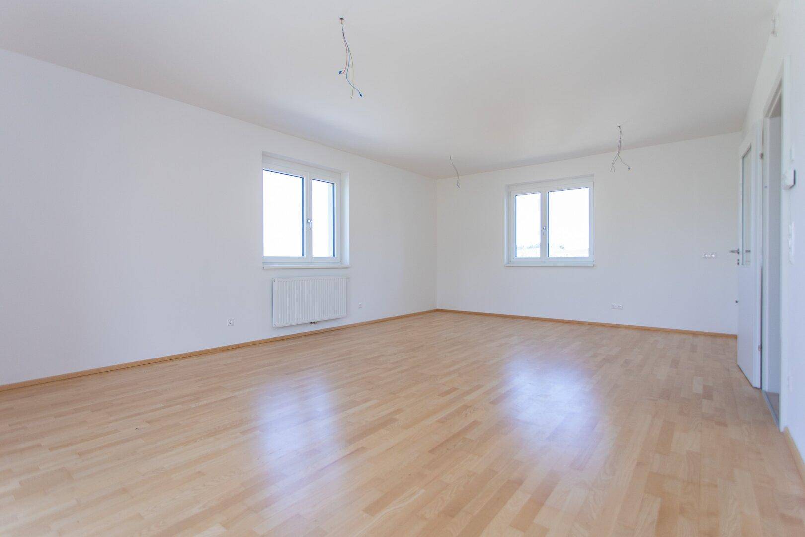 Heller Raum mit zwei Fenstern, Parkettboden und weißen Wänden, ideal für ein Wohn- oder Schlafzimmer.