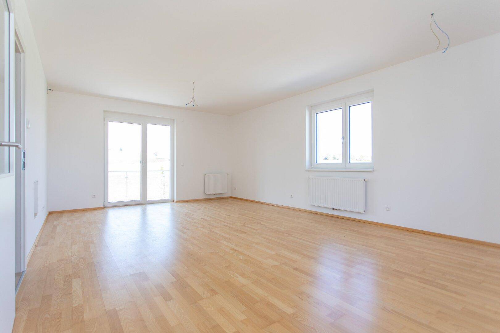 Geräumiges, helles Zimmer mit Parkettboden, weißen Wänden und großem Fenster sowie Balkonzugang.