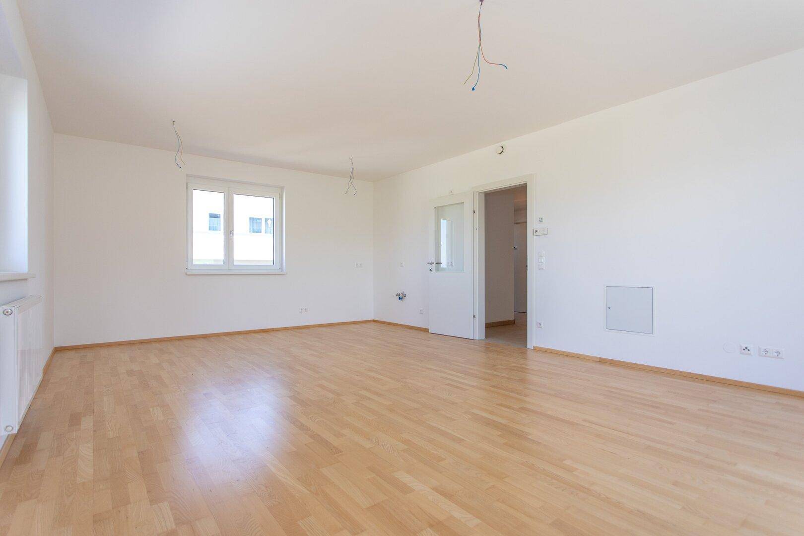 Leeres Zimmer mit hellem Parkettboden, weißen Wänden und einem Fenster, bereit zur individuellen Gestaltung.
