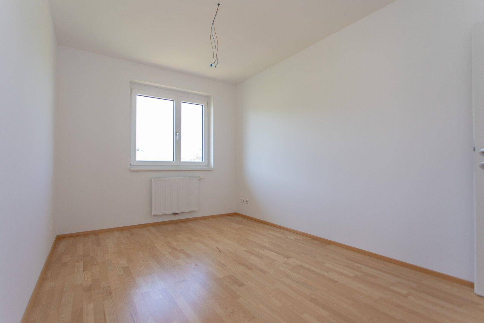 Ruhiges Schlafzimmer mit hellem Parkettboden, weißen Wänden und einem Fenster für natürliches Licht.