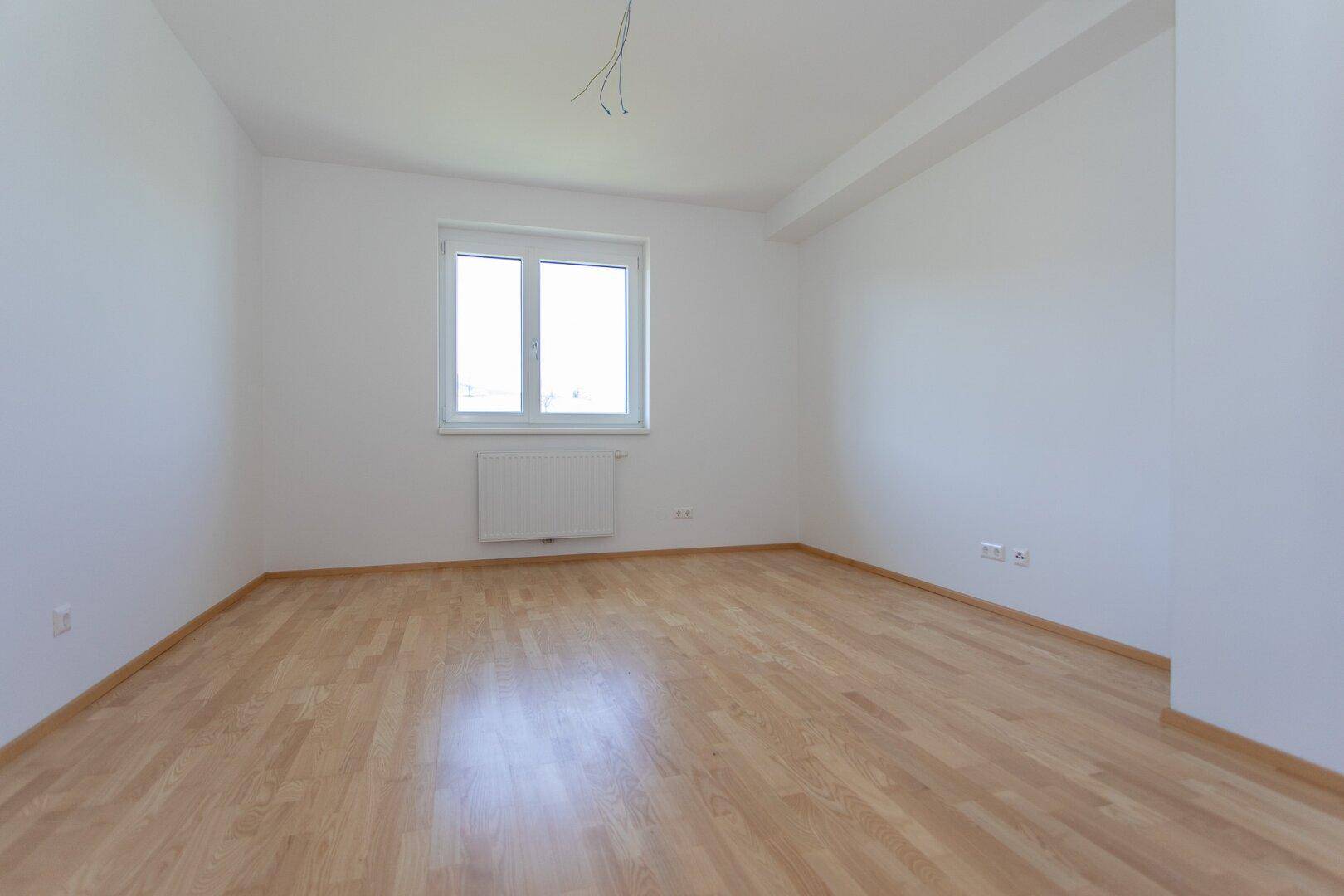 Helles Schlafzimmer mit Parkettboden und weiß gestrichenen Wänden, ausgestattet mit einem Fenster.