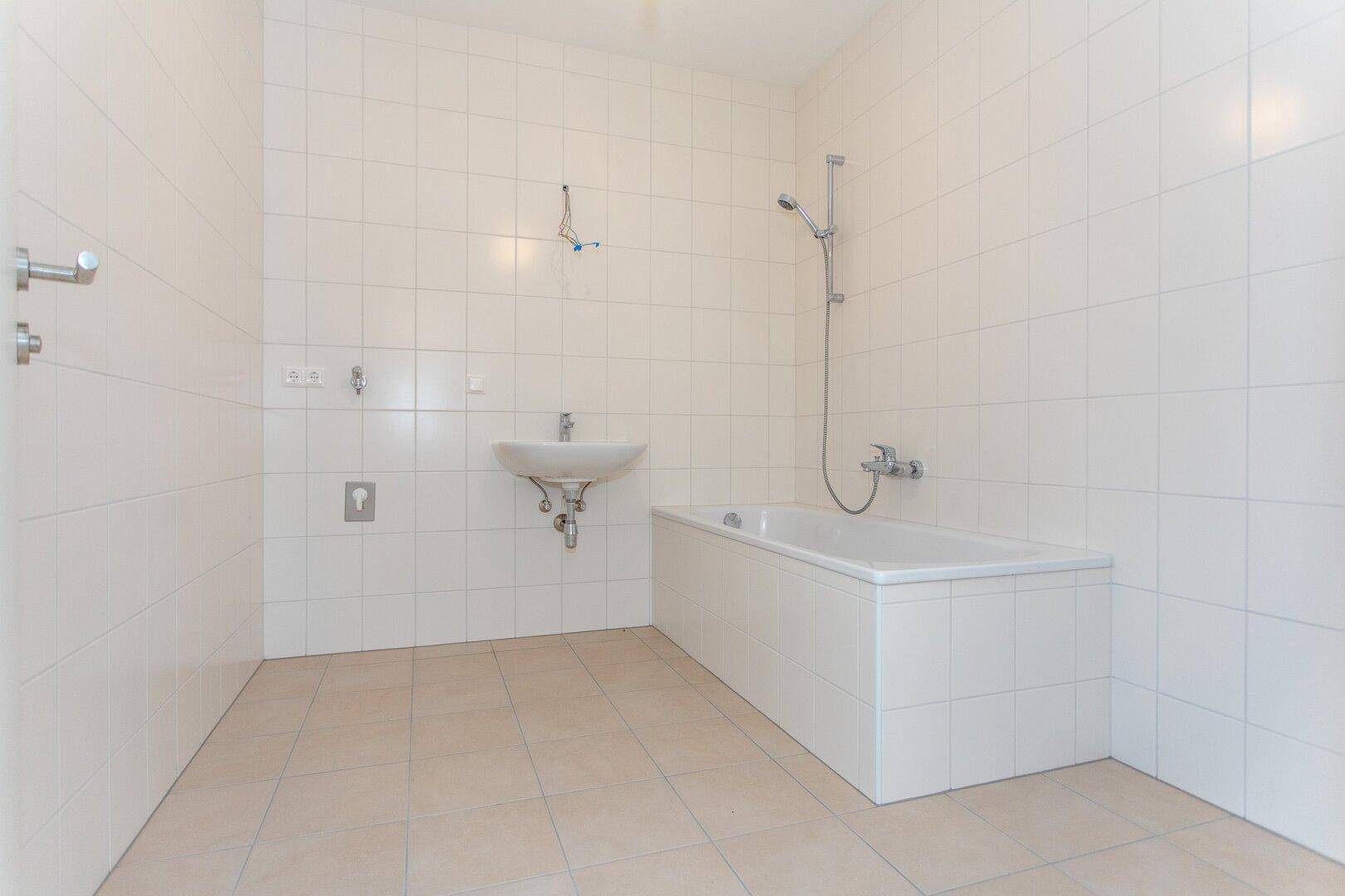 Badezimmer mit weißen Fliesen, einer Badewanne und einem einzelnen Waschbecken.