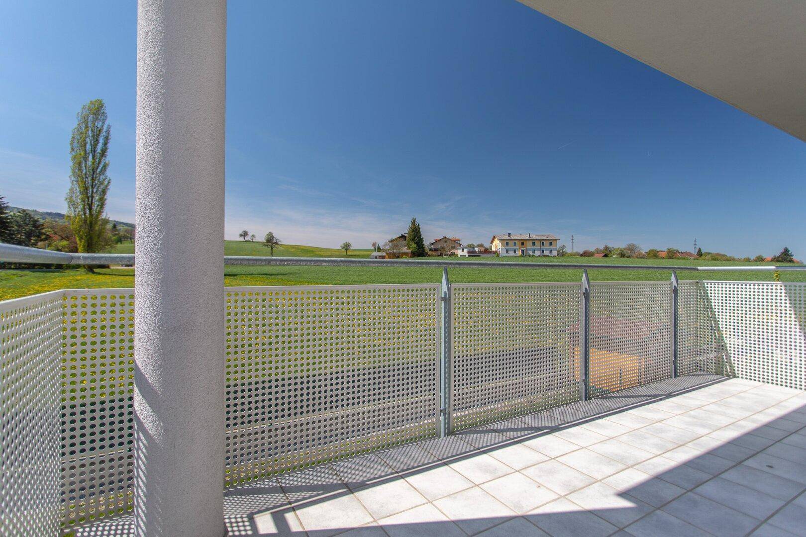 Balkon mit Blick auf weite Felder und eine ländliche Umgebung unter blauem Himmel.