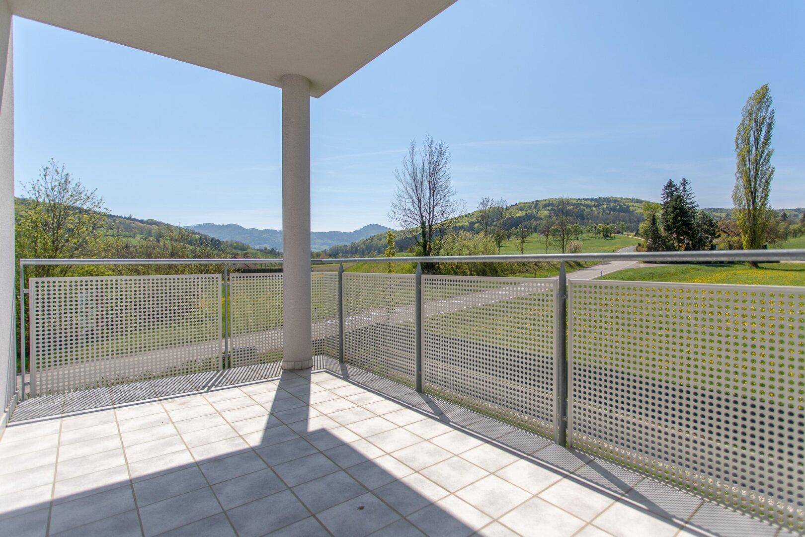 Geräumiger Balkon mit Fliesenboden und weitem Blick über die grüne Hügellandschaft.