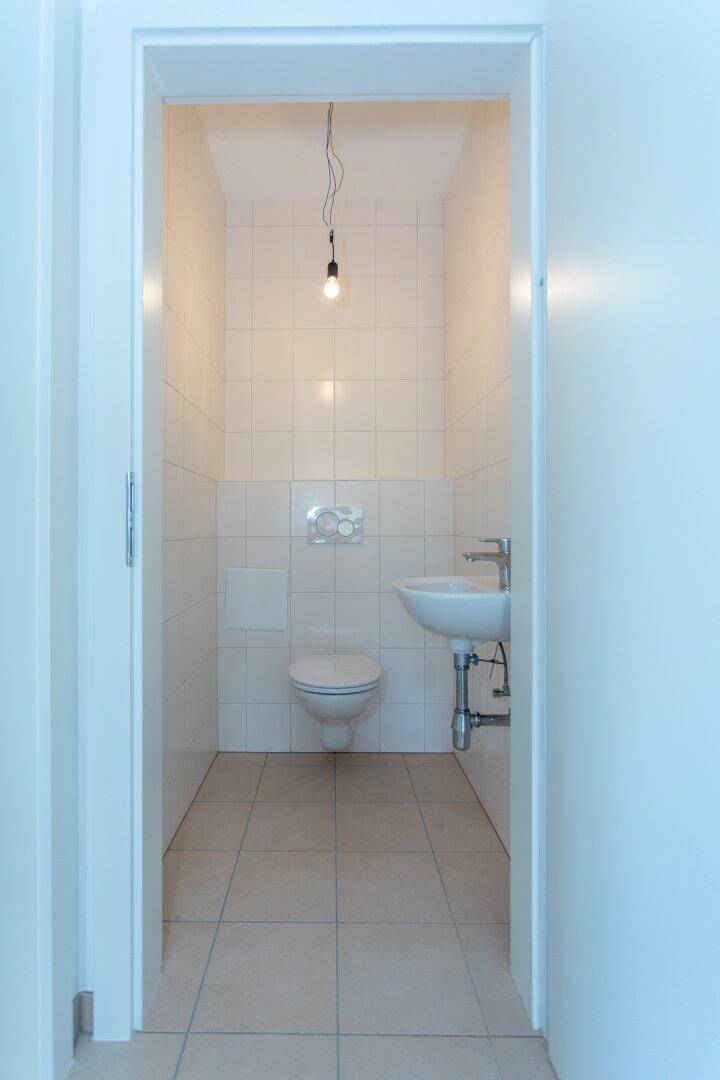 Kleines Gäste-WC mit weißen Fliesen, Toilette und einem kompakten Waschbecken.