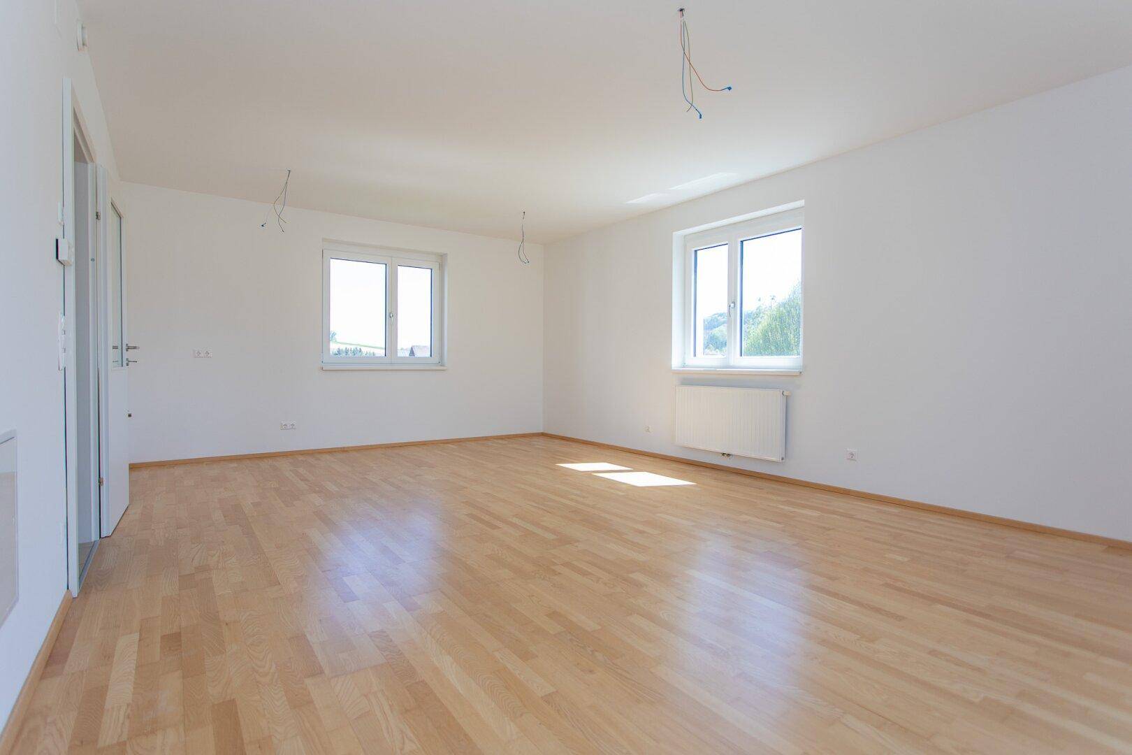 Lichtdurchfluteter Raum mit hellem Parkettboden, weißen Wänden und zwei großen Fenstern.
