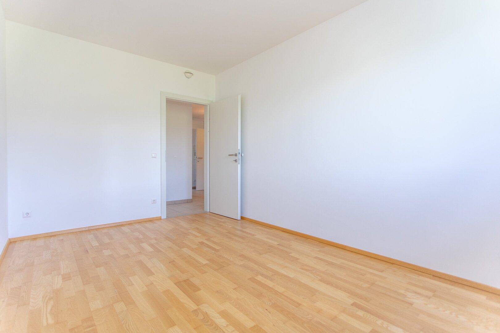 Leeres Zimmer mit hellem Parkettboden und weiß gestrichenen Wänden, bereit zur Einrichtung.