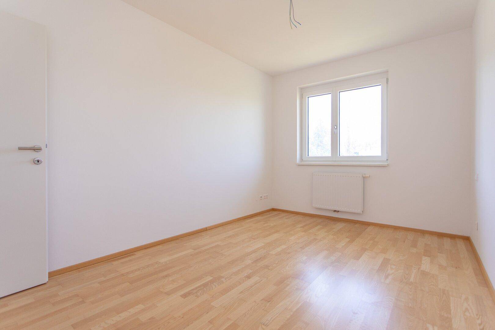 Helles Schlafzimmer mit Parkettboden, weißen Wänden und einem Fenster für natürliches Licht.