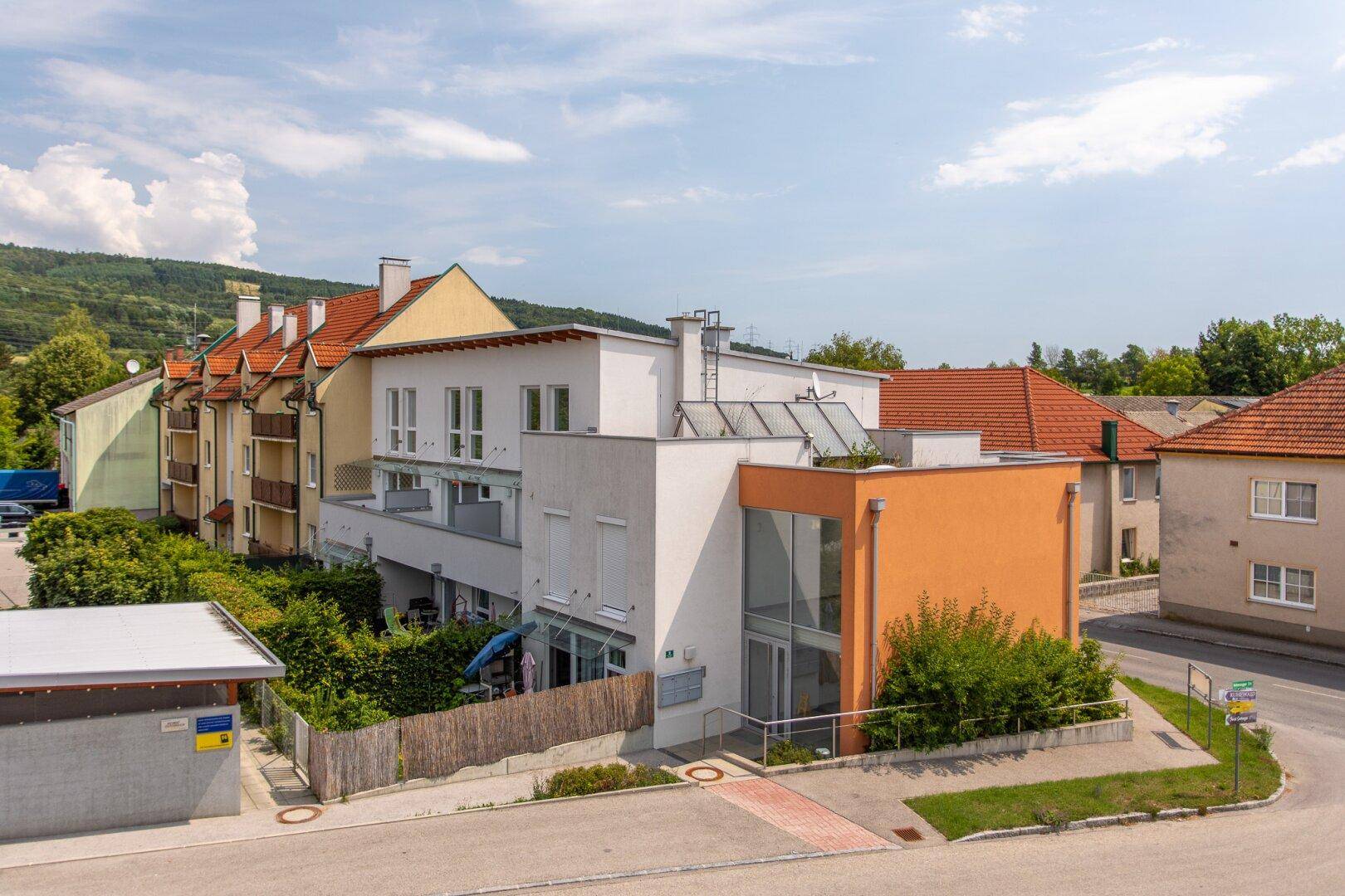 Luftaufnahme eines modernen Gebäudes mit orangefarbener Fassade und umliegenden Wohnhäusern und Grünflächen.