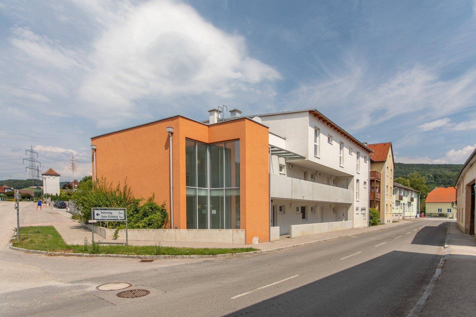 Modernes Gebäude mit orangefarbener und weißer Fassade an einer Straße unter blauem Himmel.
