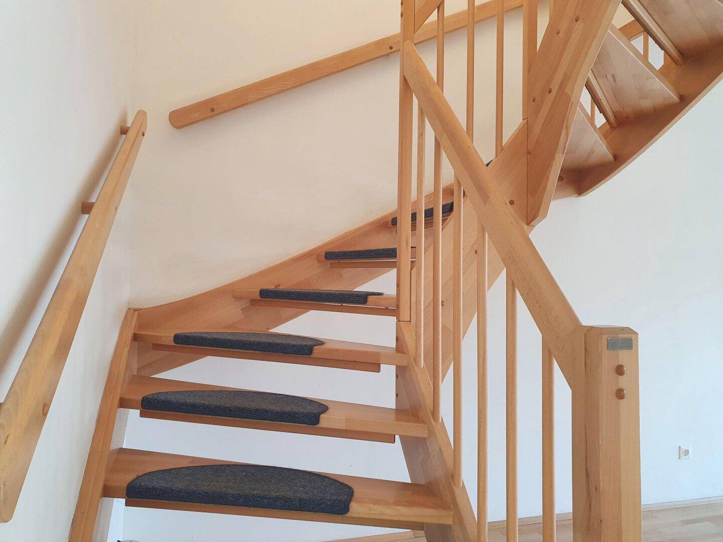 Helle Holztreppe mit Teppichstufen und Holzgeländer, die verschiedene Etagen in einem Wohnhaus verbindet.