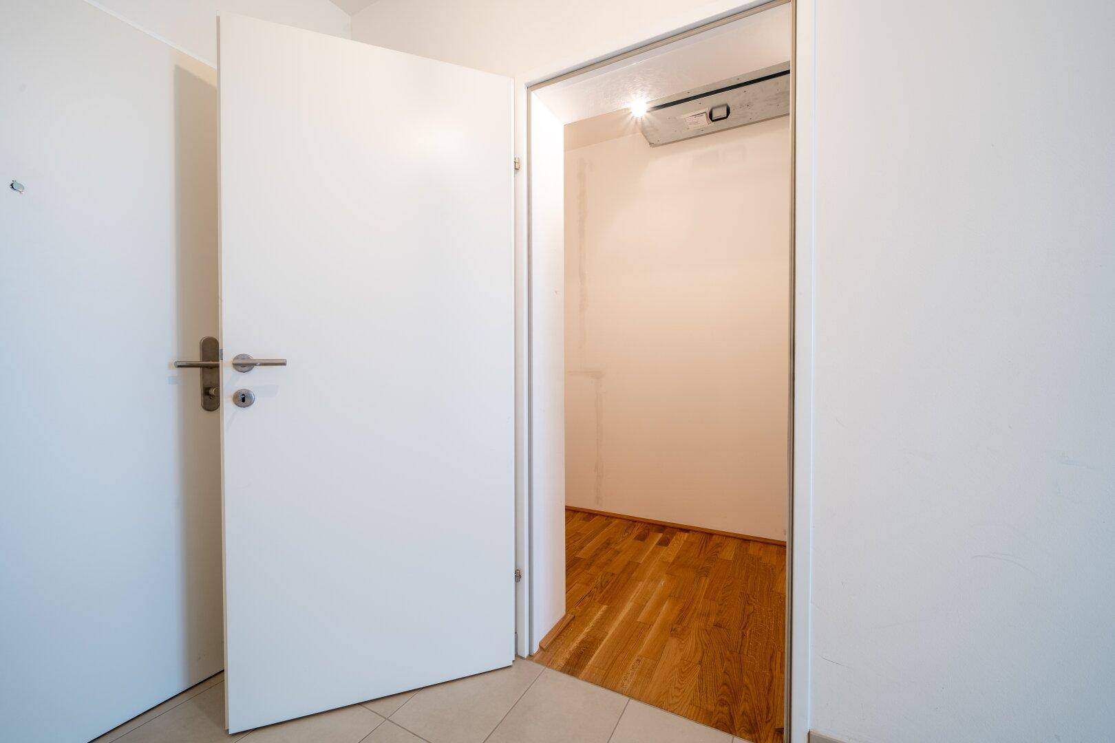 Heller Flur mit Fliesenboden und einer offenen Tür, die den Blick in einen weiteren Raum freigibt.