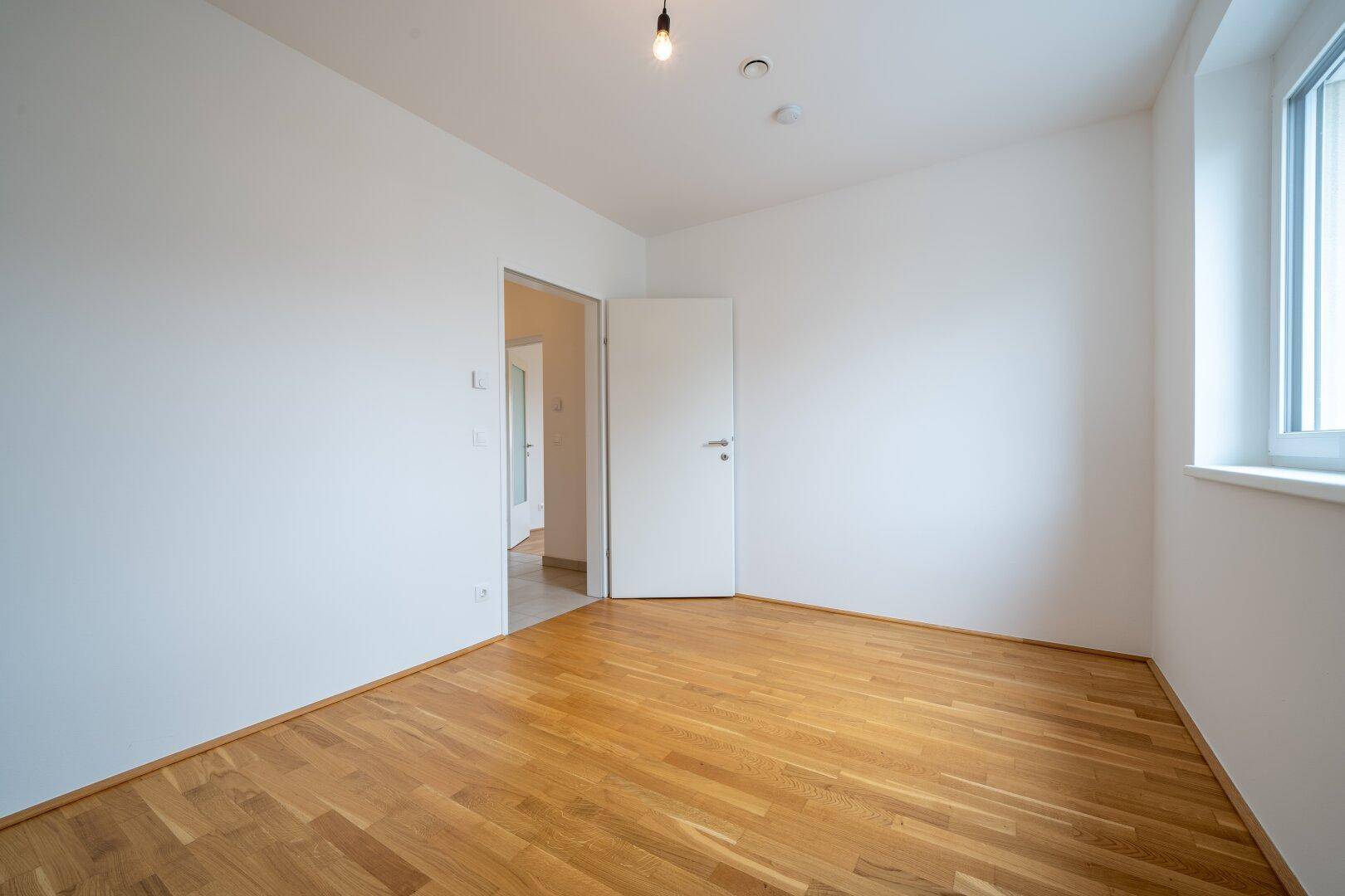 Geräumiges Schlafzimmer mit Parkettboden und einer Tür, die zu einem weiteren Raum führt.