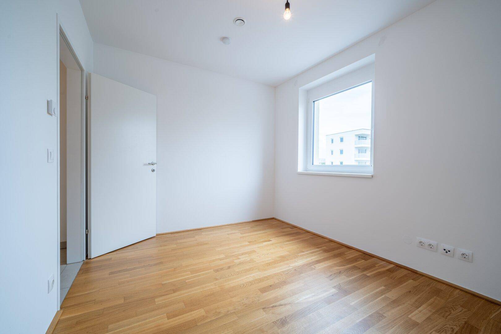 Helles Zimmer mit Parkettboden und einem Fenster, das viel Tageslicht in den Raum bringt.