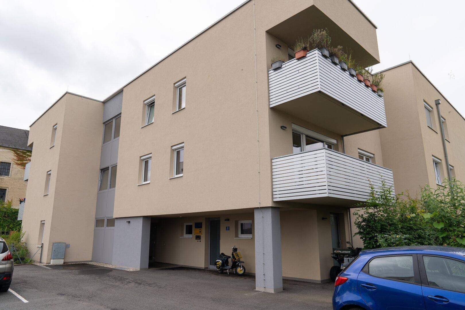 Modernes Mehrfamilienhaus mit Balkonen und beiger Fassade in städtischer Umgebung.