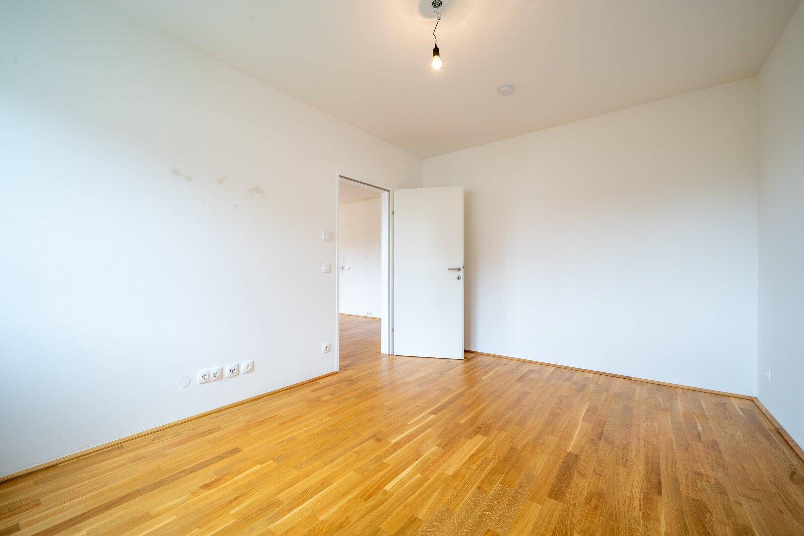 Helles Schlafzimmer mit Parkettboden und einer Tür, die den Zugang zu anderen Räumen ermöglicht.