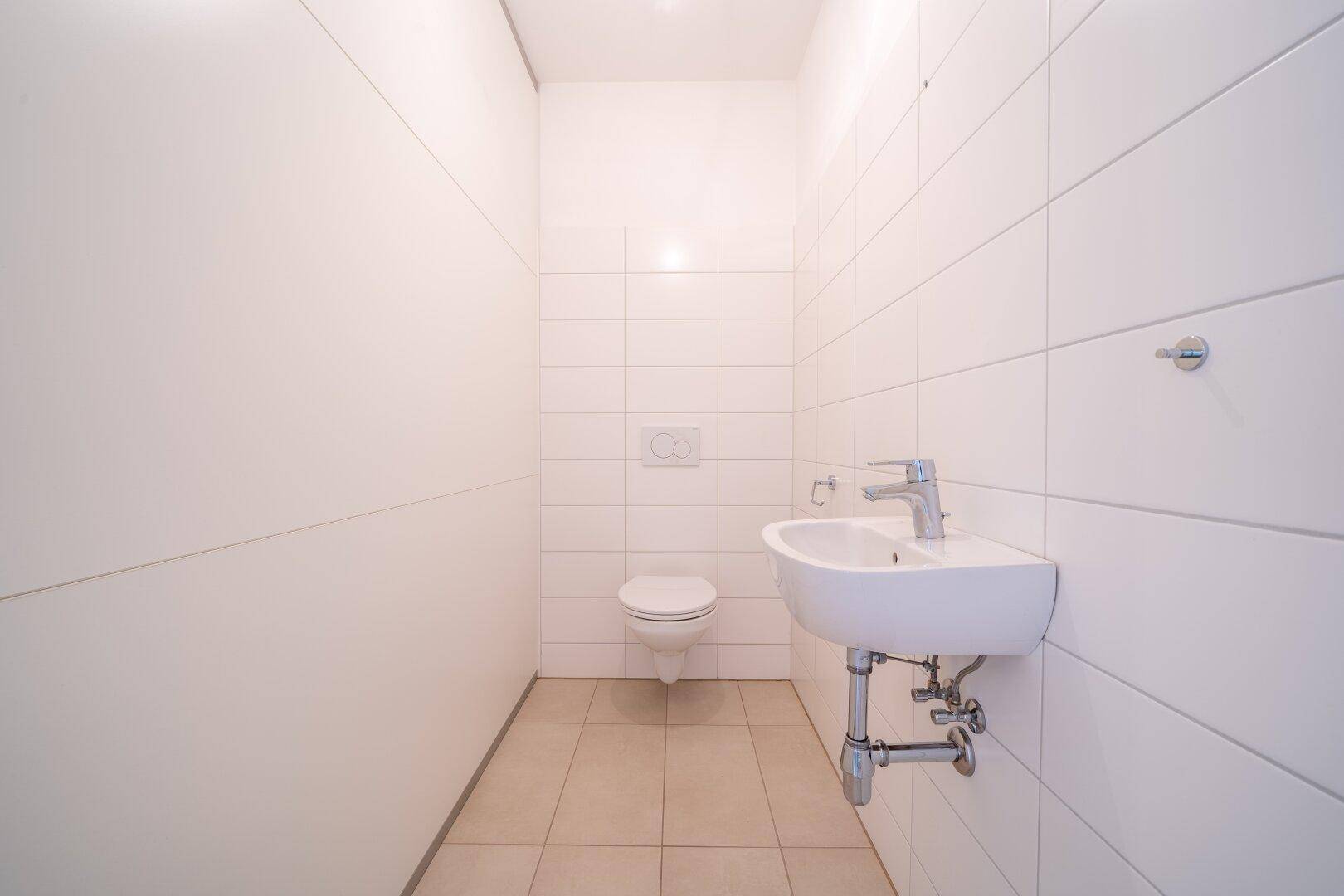Separates Gäste-WC mit wandhängender Toilette, kleinem Waschbecken und weißen Fliesen.