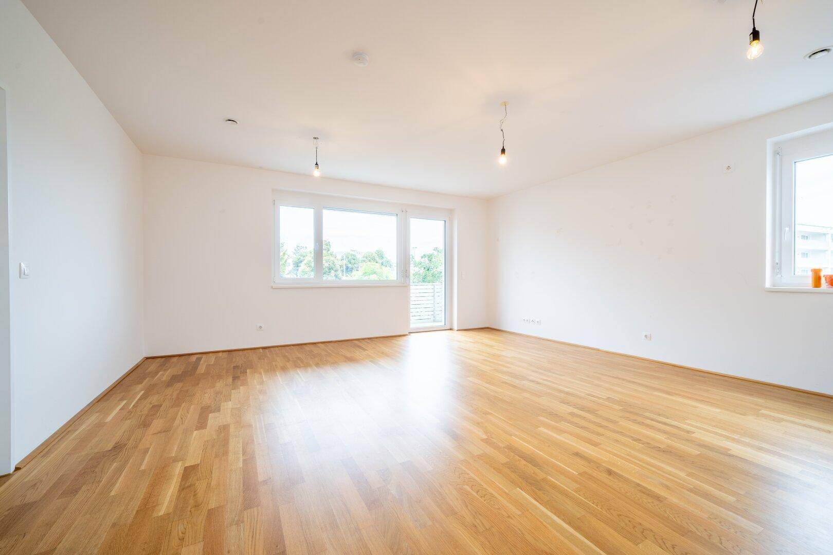 Heller Wohnbereich mit Parkettboden und großen Fenstern, die den Raum mit Licht füllen.