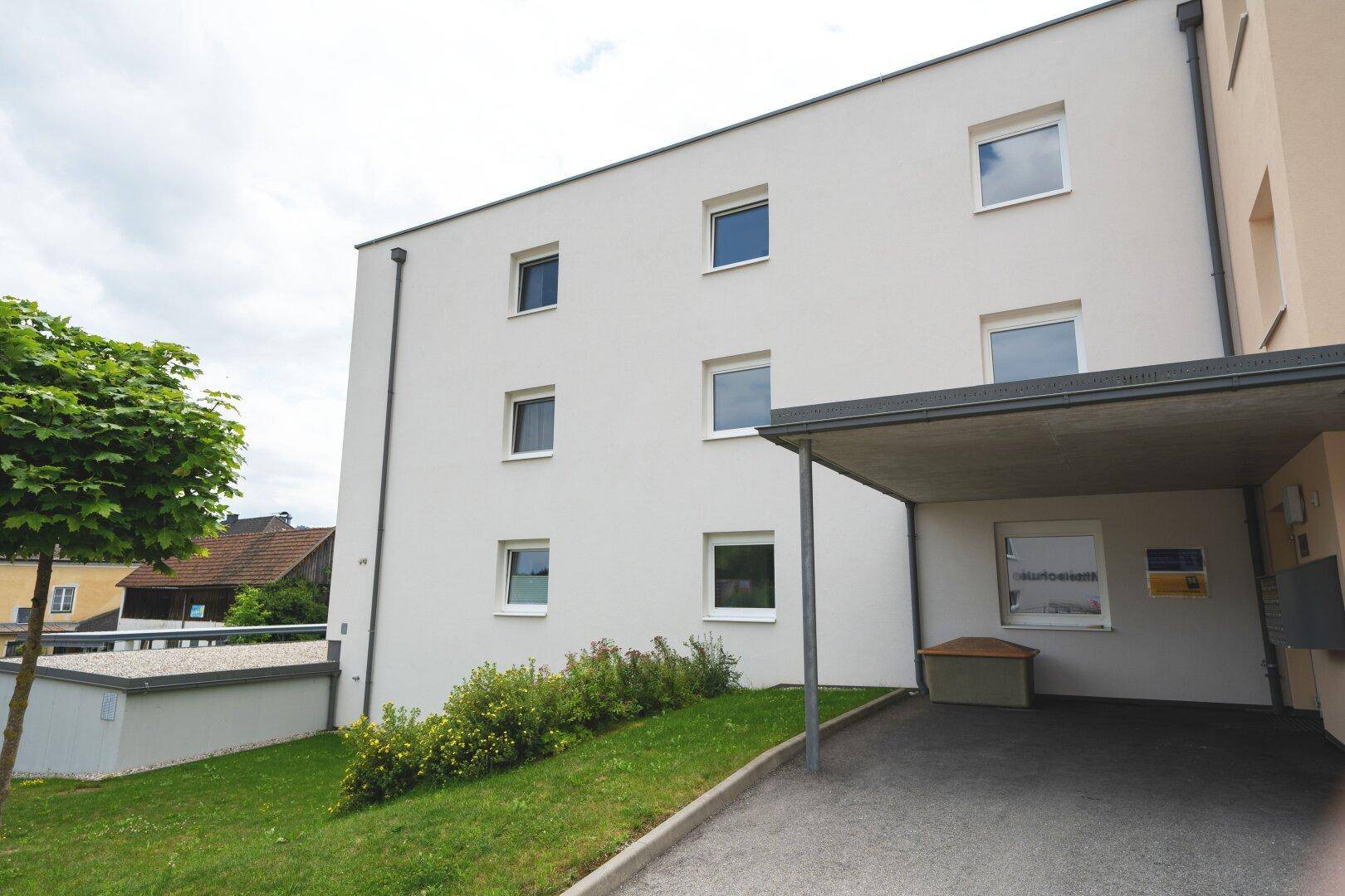 Moderne Fassade eines Mehrfamilienhauses mit Carport und gepflegter Grünfläche im Vordergrund.