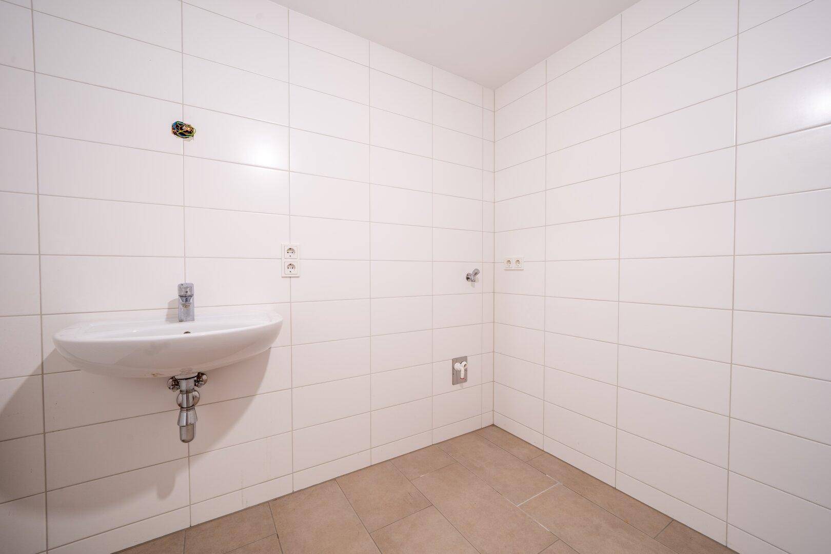 Kleiner Raum mit weißen Wandfliesen, beigem Boden und einem Waschbecken, ideal als Gäste-WC.