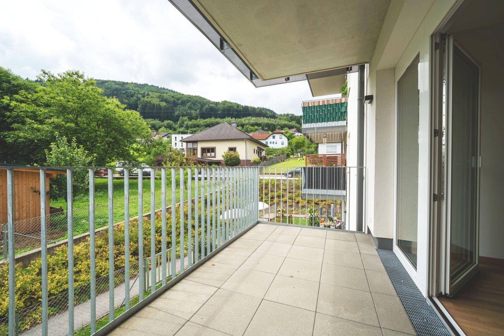 Heller Balkon mit Metallgeländer und weitem Blick auf die grüne Umgebung und Häuser.