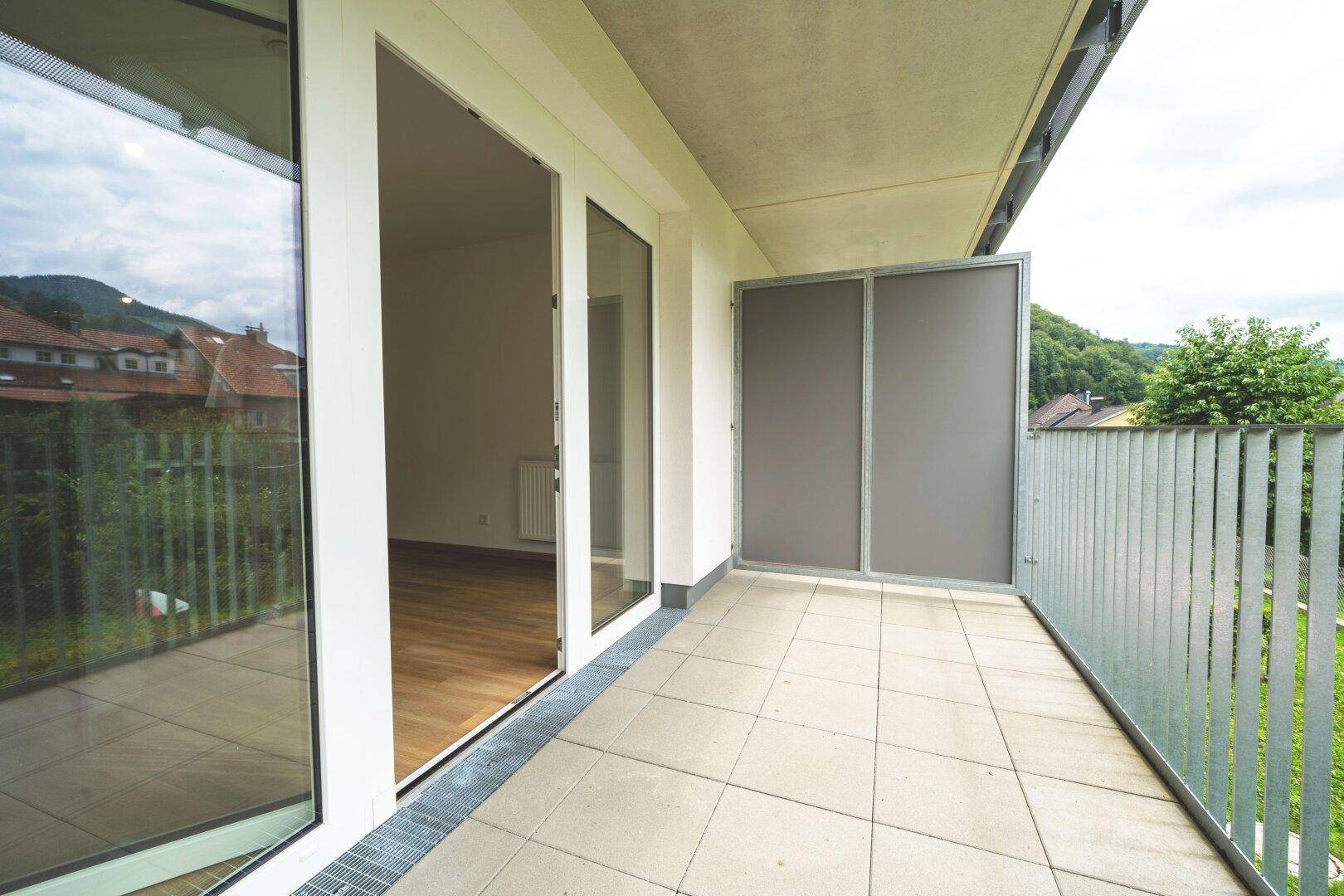 Balkon mit Fliesenboden, Glasschiebetüren zum Innenraum und seitlichem Sichtschutz.