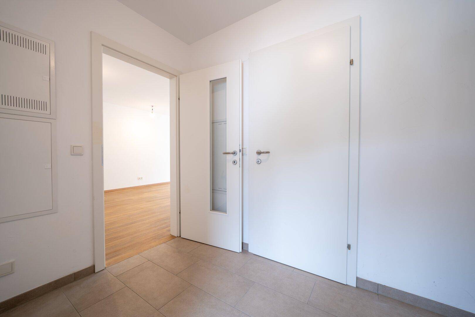 Heller Flur mit Fliesenboden und modernen weißen Türen, eine davon mit Glaseinsatz.