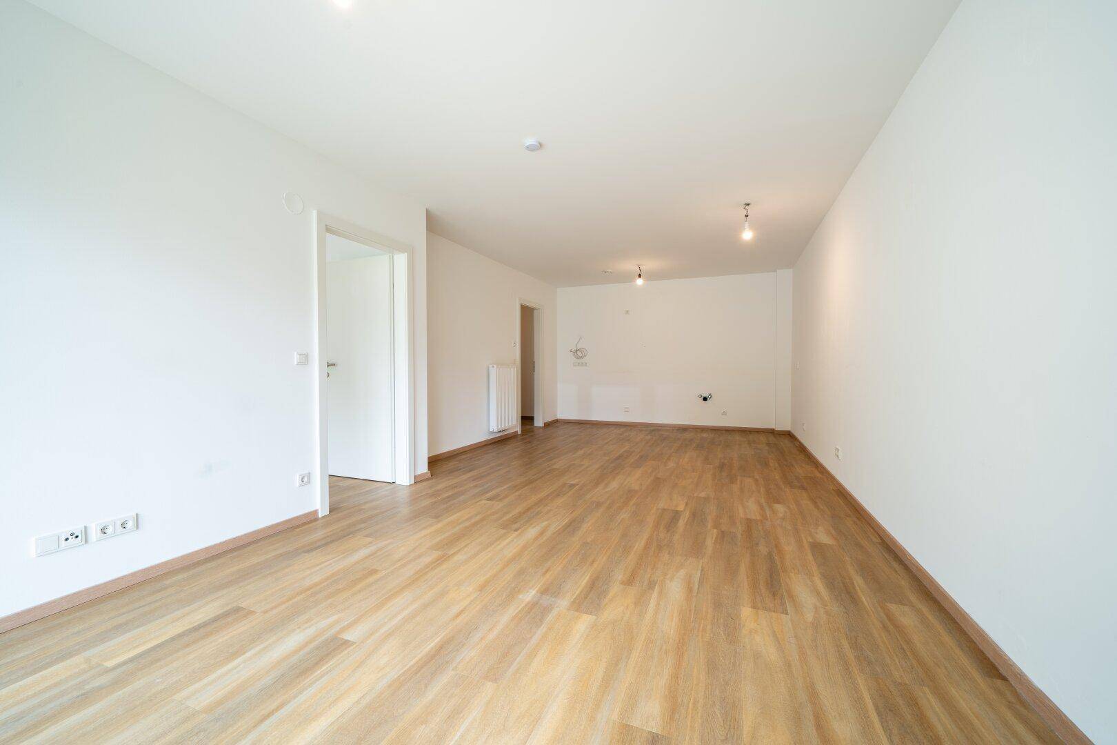 Geräumiger, heller Raum mit Holzboden und weiß gestrichenen Wänden, bereit zur Einrichtung.