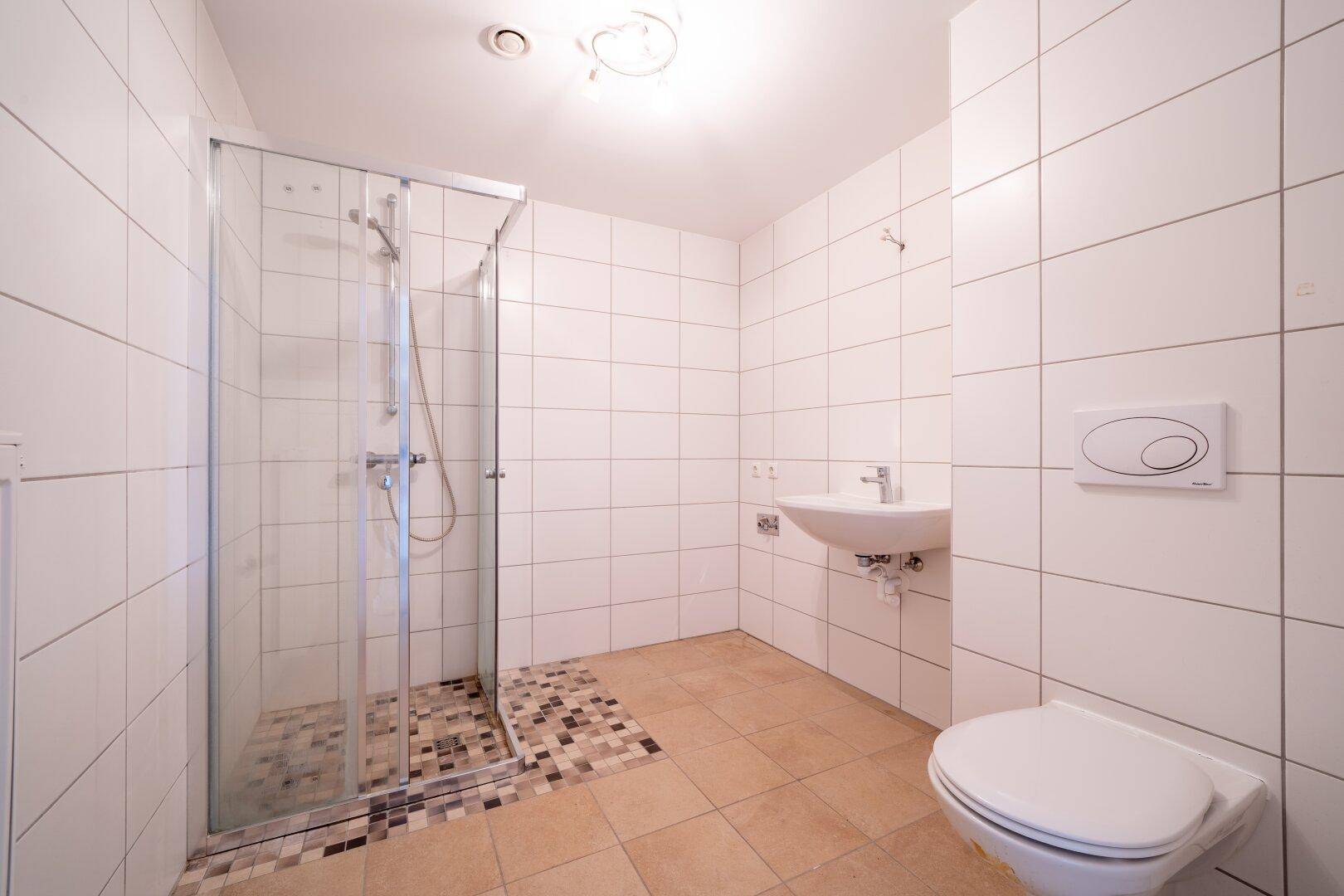 Modernes Badezimmer mit Duschkabine, wandhängendem WC und Waschbecken, hell gefliest.