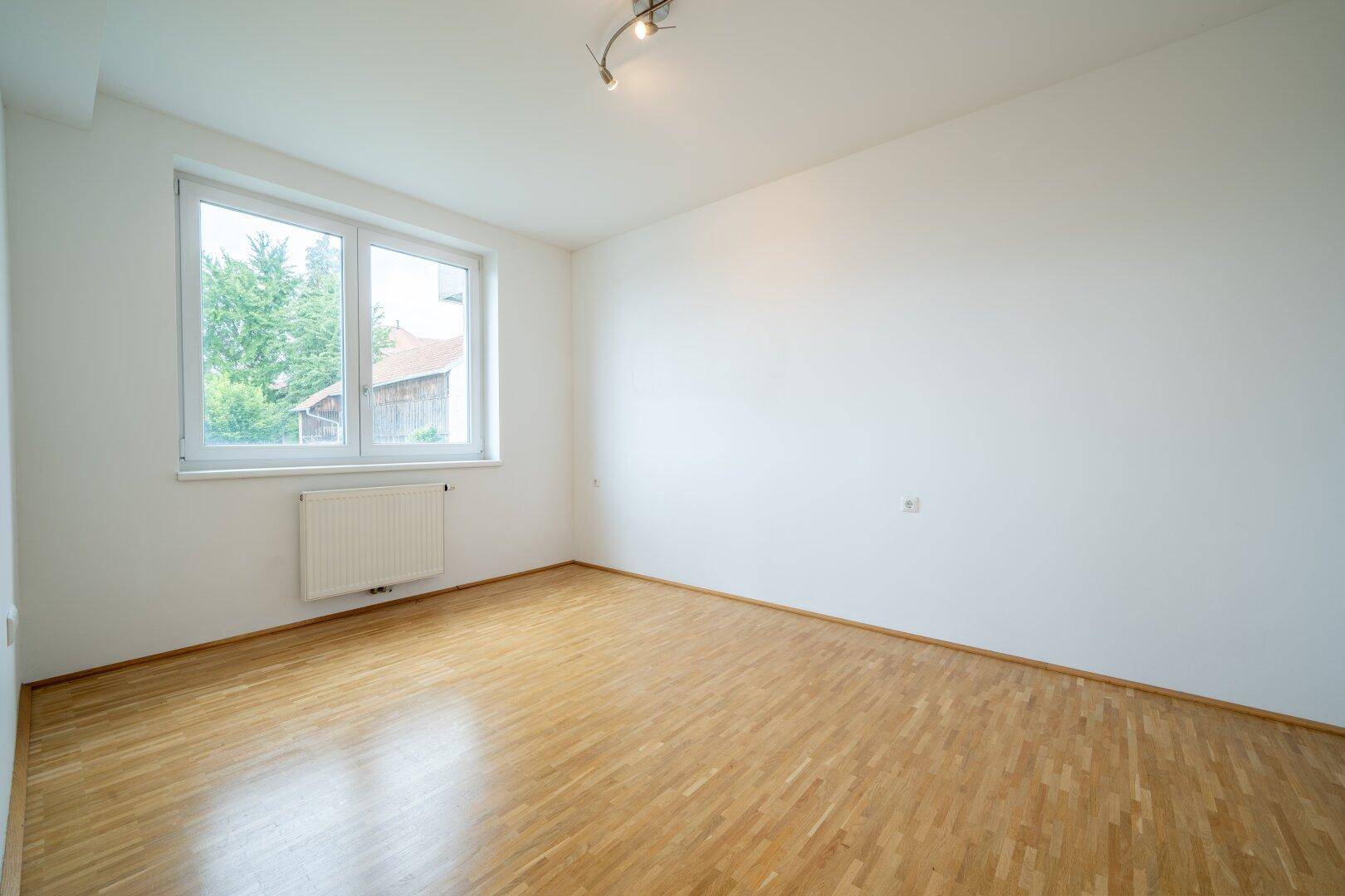 Ruhiges Schlafzimmer mit Parkettboden und großem Fenster, bietet einen Blick ins Grüne.