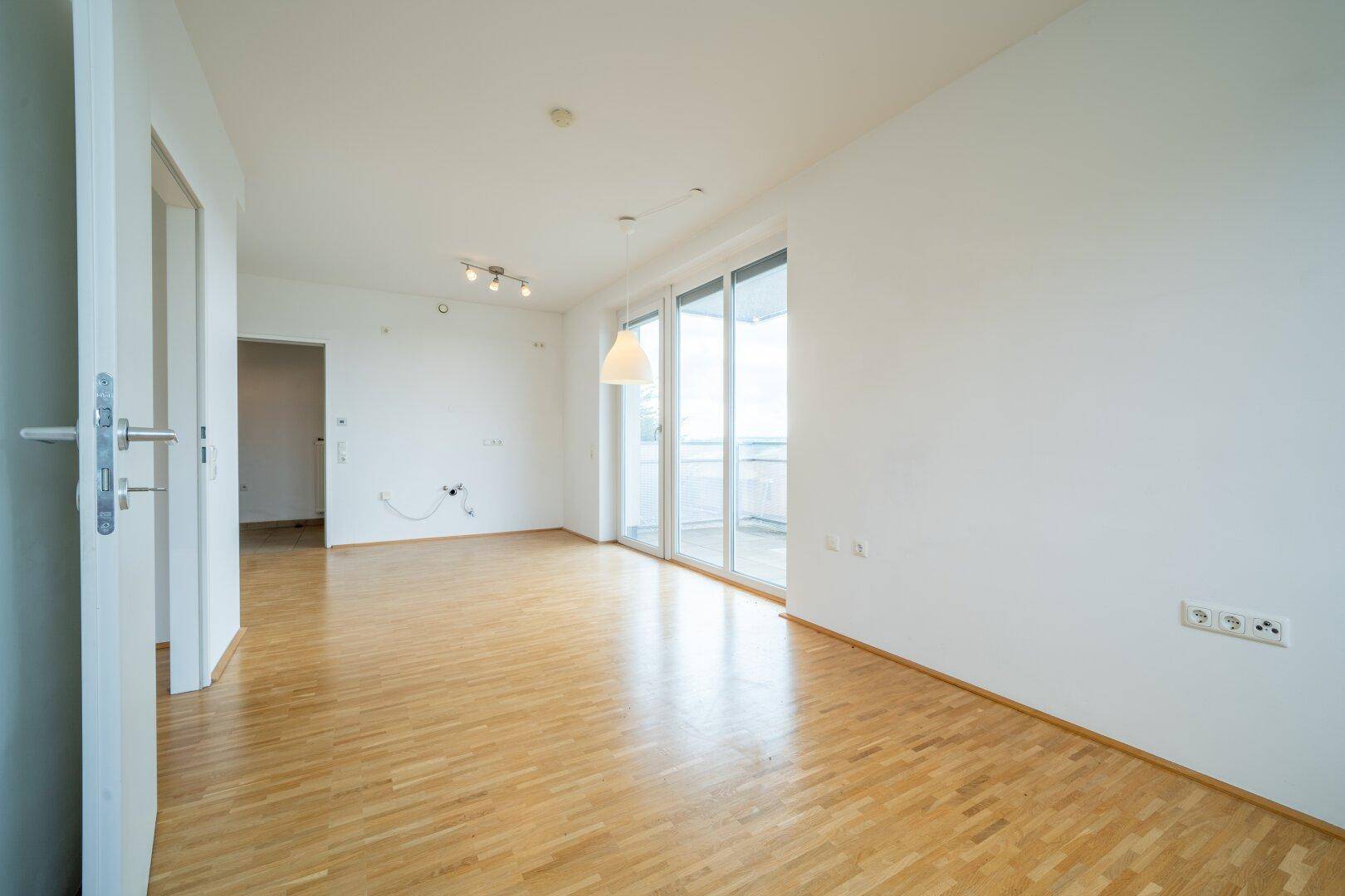 Geräumiges Zimmer mit Holzboden und Zugang zu einem Balkon, ideal für offene Gestaltung.