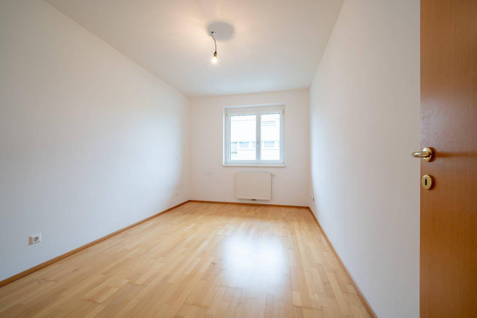 Gemütliches Schlafzimmer mit hellem Parkettboden und einem Fenster, das viel Tageslicht hereinlässt.