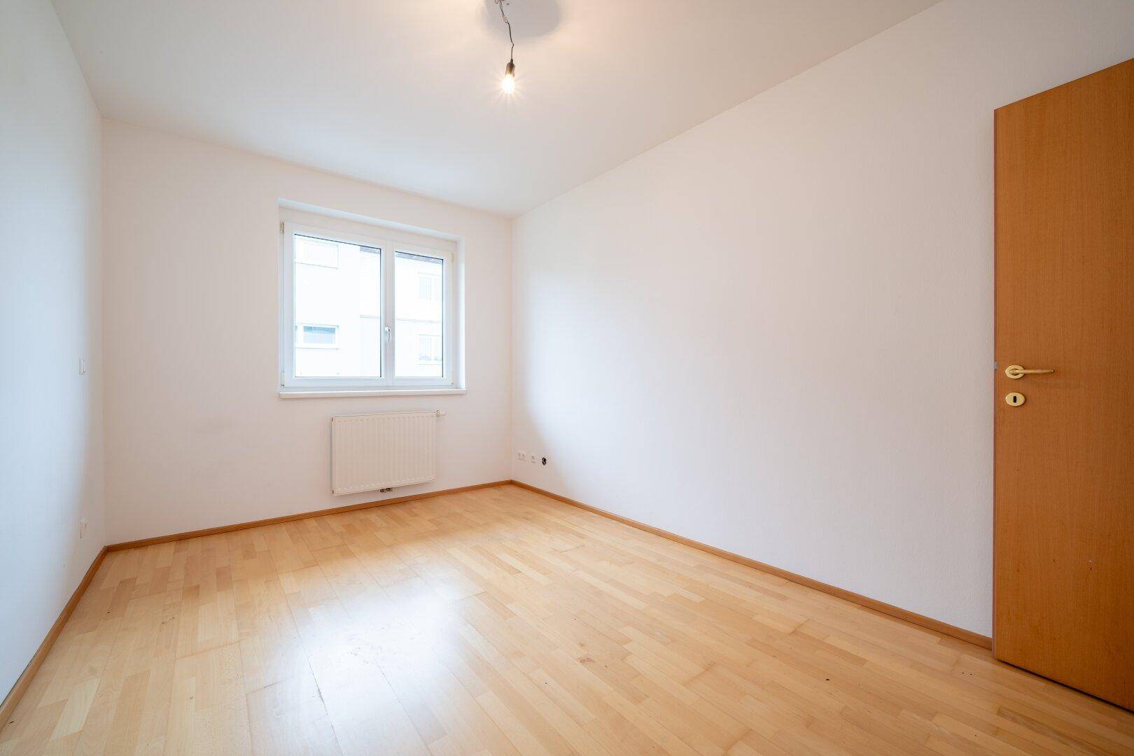 Helles Schlafzimmer mit Parkettboden und einem Fenster, das eine angenehme Atmosphäre schafft.