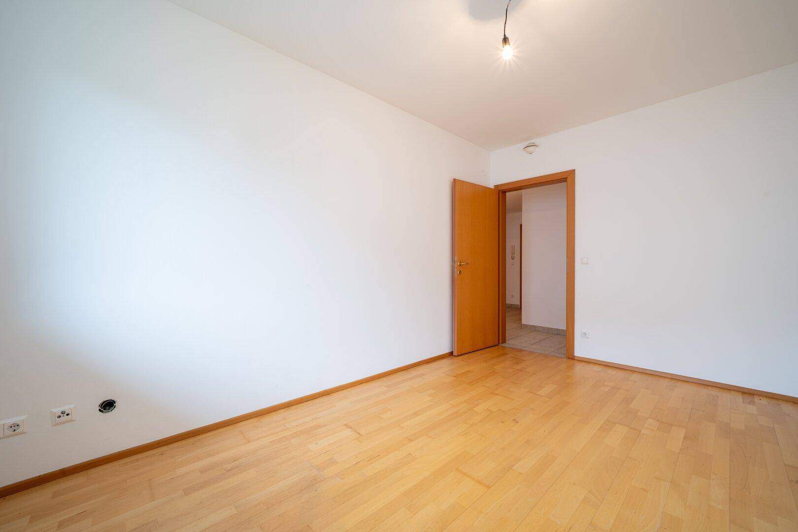 Leeres Schlafzimmer mit Parkettboden und einer Holztür, bereit für neue Bewohner.
