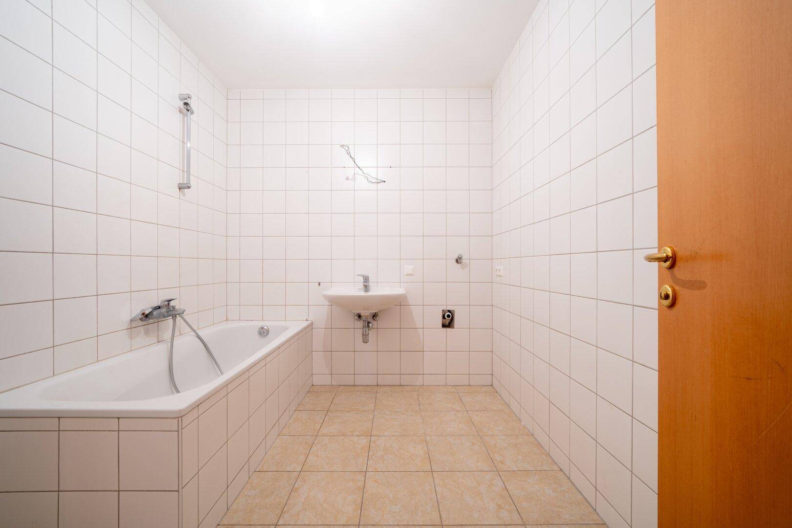 Gefliestes Badezimmer mit Badewanne und Waschbecken, bereit für die Installation weiterer Armaturen.