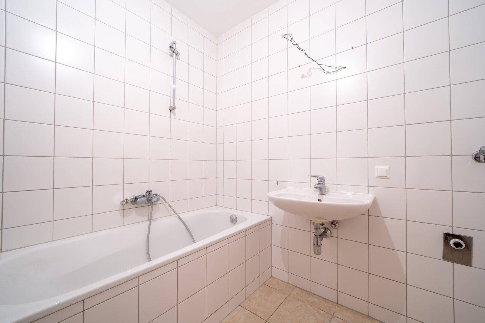 Helles Badezimmer mit weißen Fliesen, Badewanne und Waschbecken, in gutem Zustand.