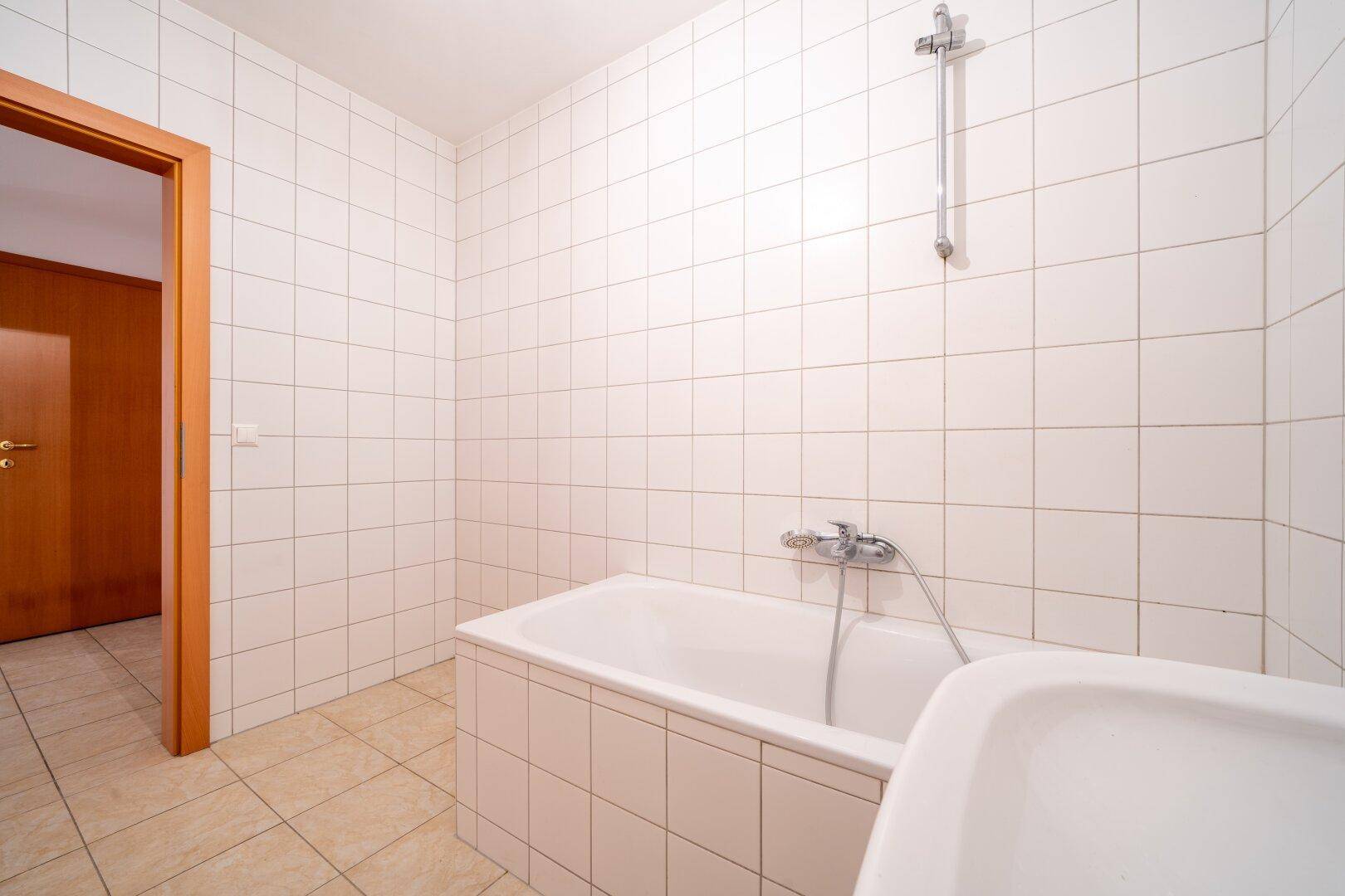 Badezimmer mit Badewanne und Waschbecken, komplett gefliest und gut gepflegt.