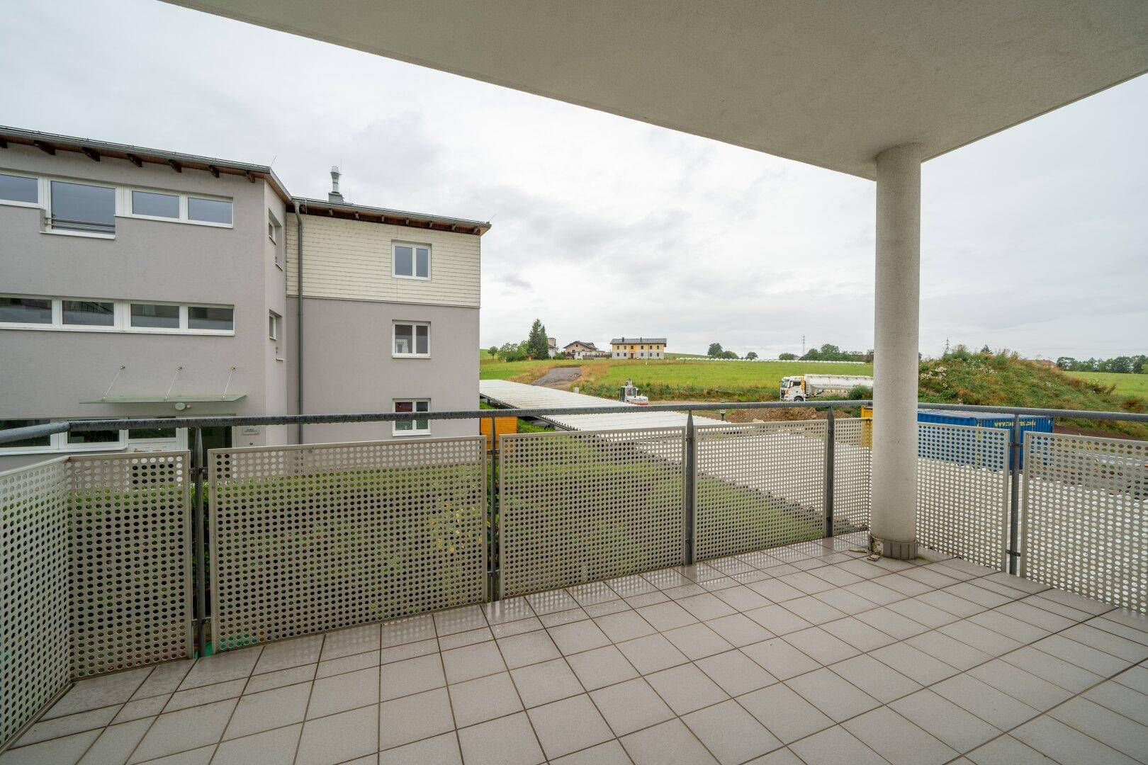 Geräumiger Balkon mit Fliesenboden und Blick auf die grüne Umgebung und ein Gebäude.