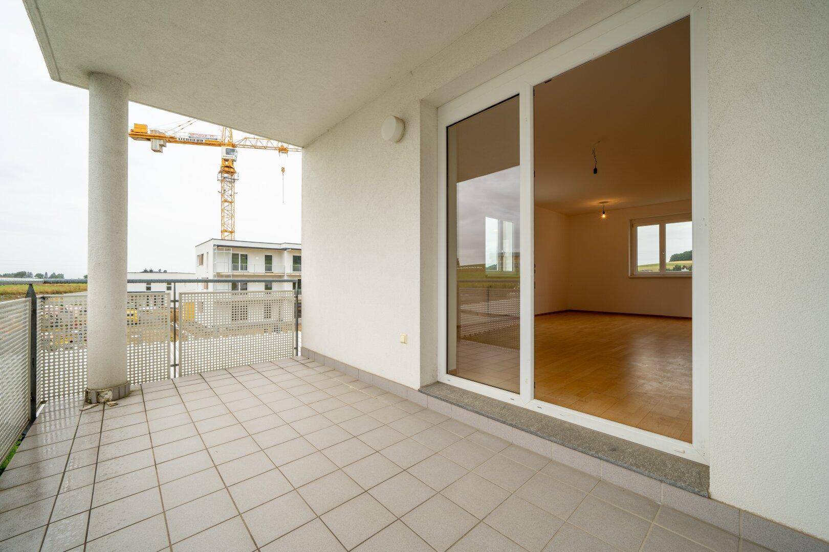 Balkon mit Fliesenboden und Blick auf eine Baustelle und die ländliche Umgebung.
