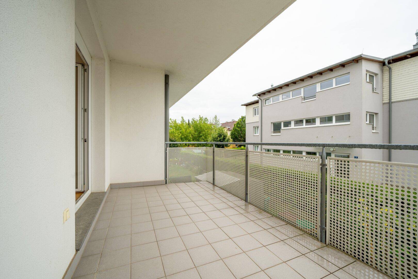Heller Balkon mit Fliesenboden und Blick auf die umliegenden Gebäude und Bäume.