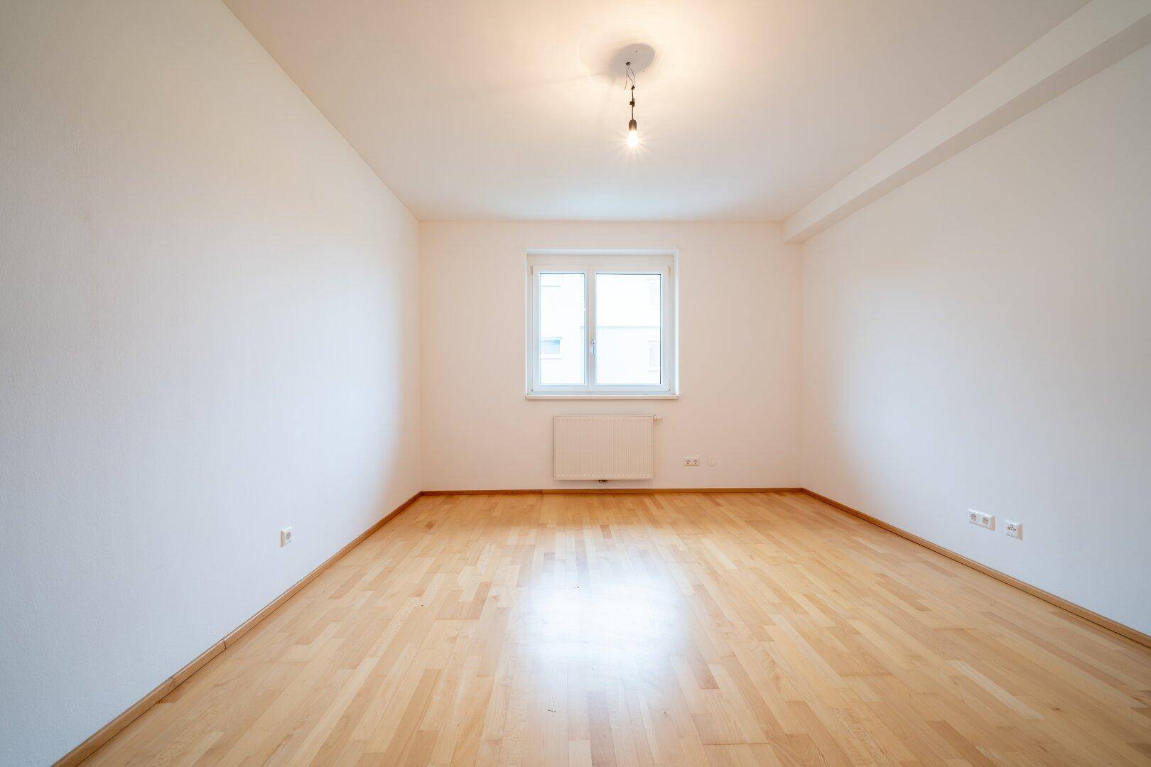 Helles Schlafzimmer mit Parkettboden und einem Fenster, das für gute Belüftung sorgt.