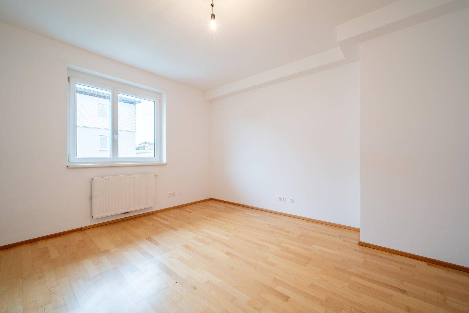 Geräumiges Schlafzimmer mit Parkettboden und einem Fenster, das viel Tageslicht bietet.
