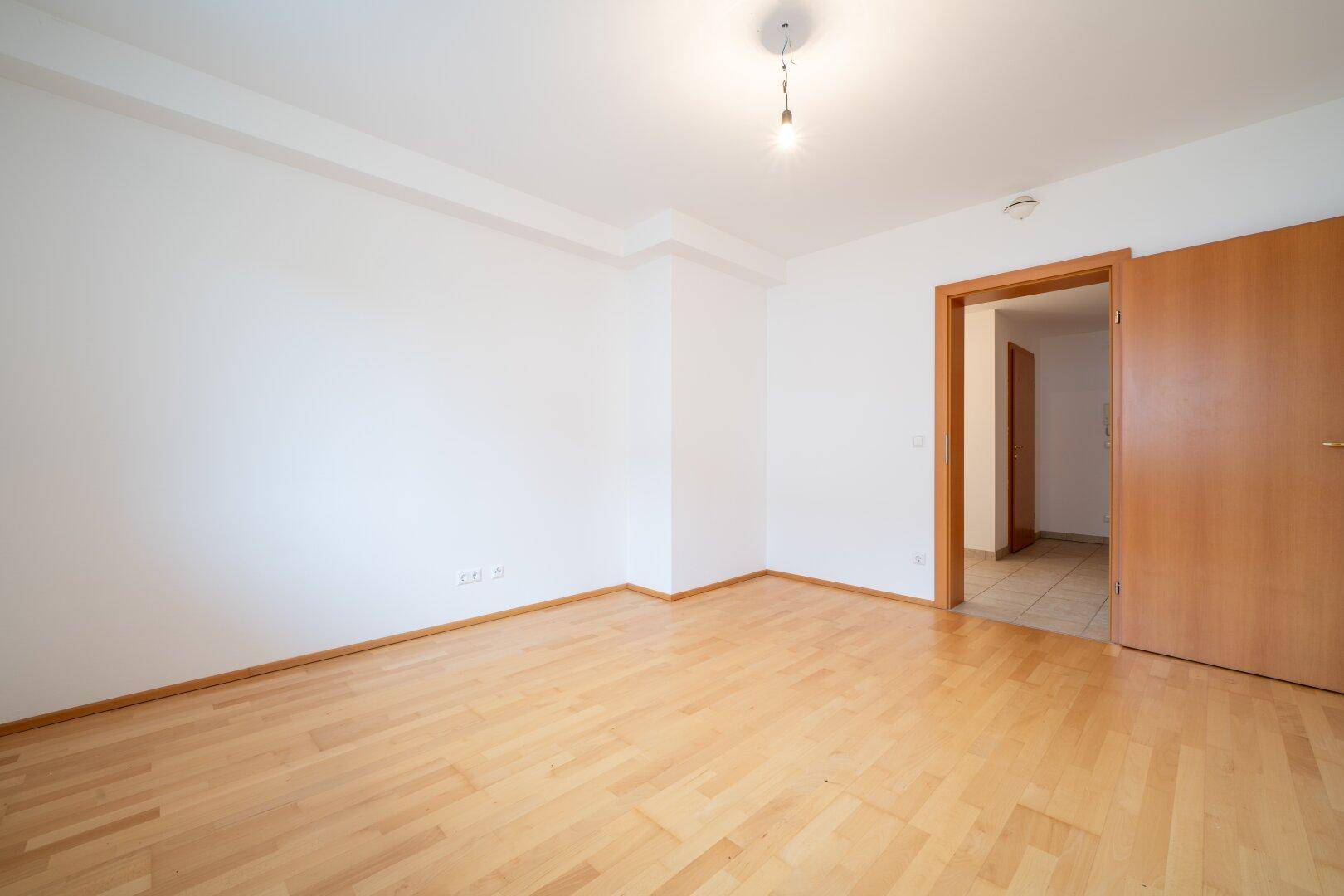 Leeres Schlafzimmer mit Parkettboden und einer Holztür, ideal für individuelle Einrichtungsideen.