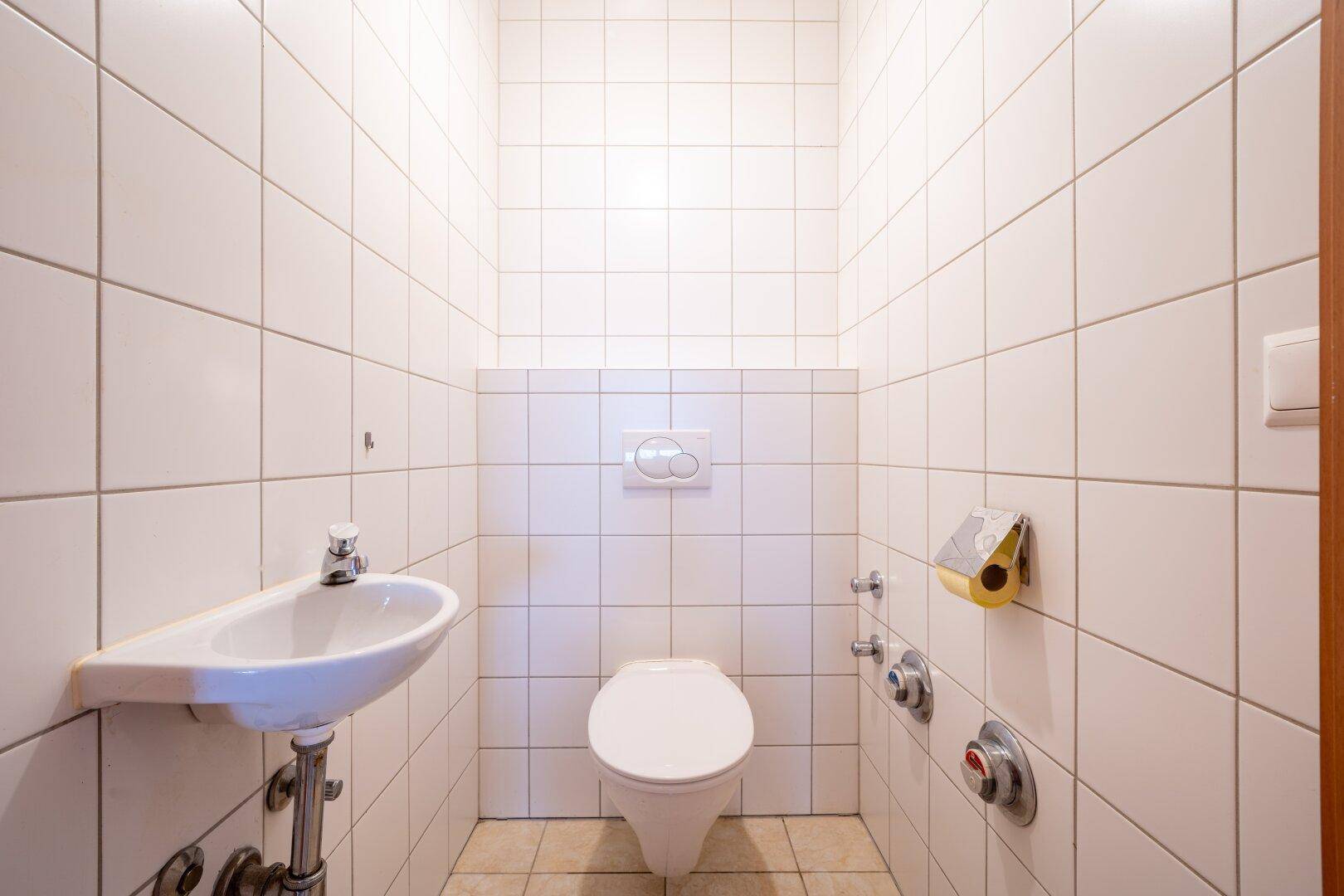 Separates WC mit wandhängender Toilette und kleinem Handwaschbecken, komplett gefliest.