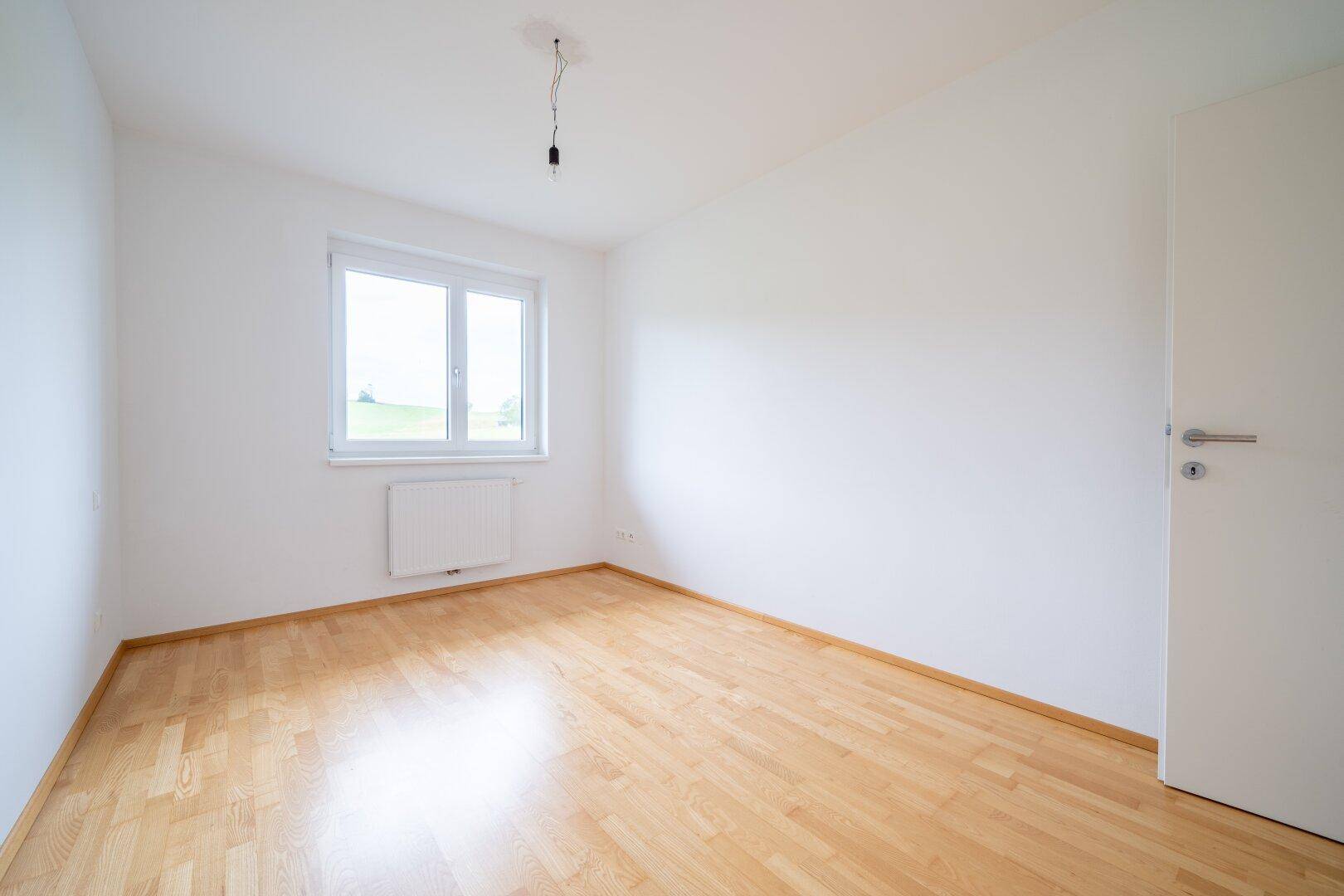 Freundliches Schlafzimmer mit Parkettboden und weiß gestrichenen Wänden, bereit zur individuellen Gestaltung.