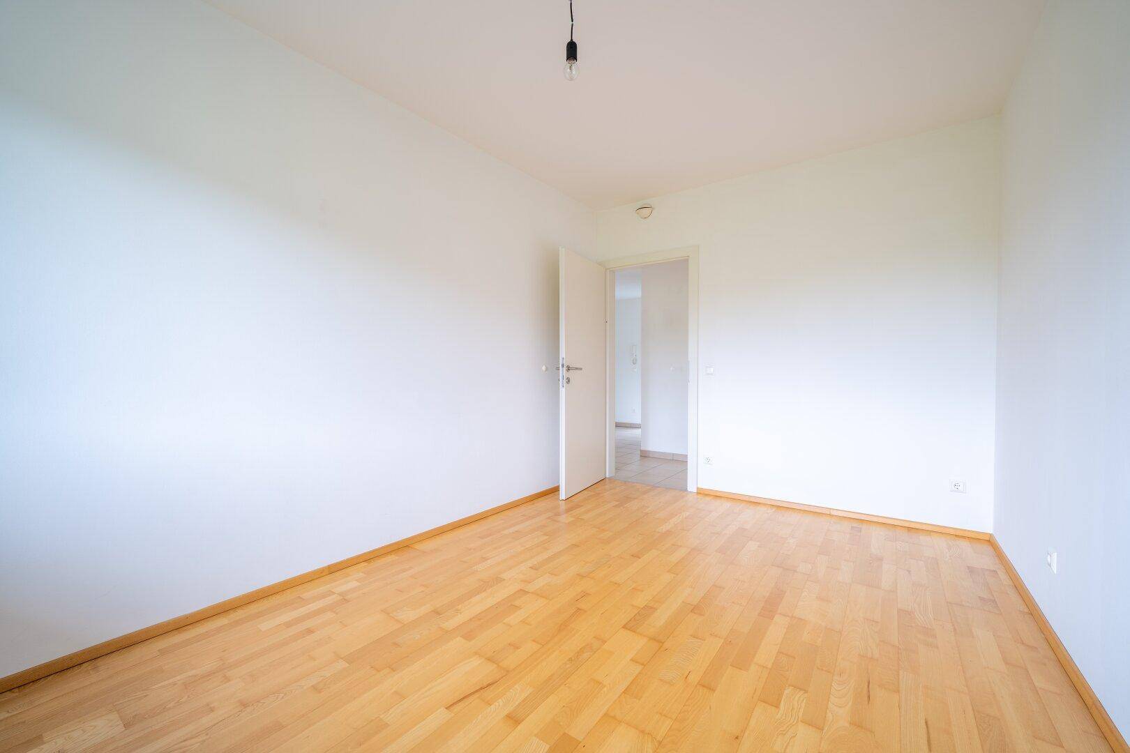 Helles Schlafzimmer mit Parkettboden und Zugang zu einem weiteren Raum, ideal für ein Kinderzimmer.