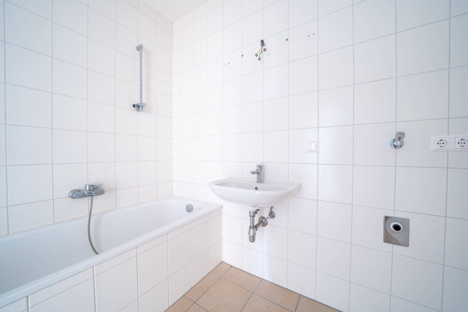 Funktionales Badezimmer mit weißen Fliesen, Badewanne und Waschbecken, bereit zur Modernisierung.