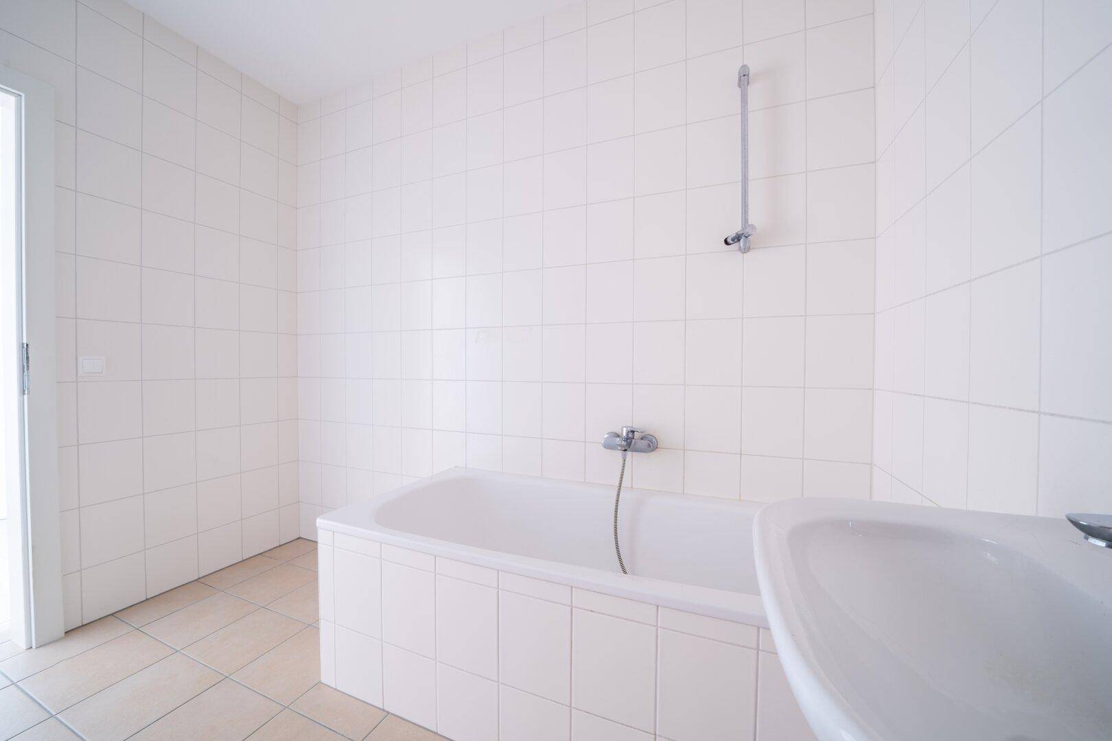 Badezimmer mit Badewanne und Waschbecken, komplett gefliest in neutralem Weiß, bietet Potenzial.